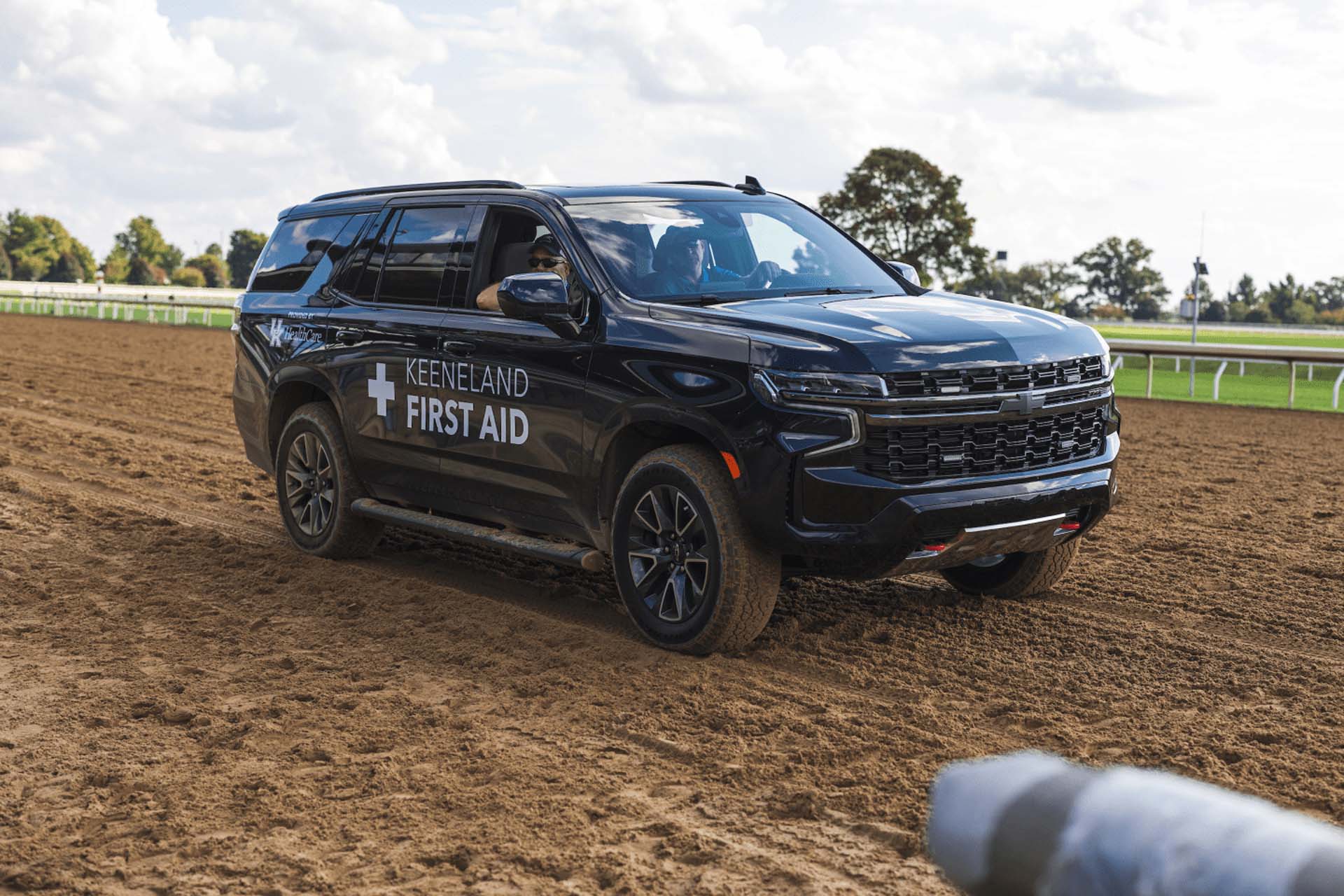 A picture of the Racetrackelite First Aid car on the dirt track. It is a large black Chevy SUV.